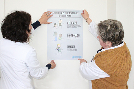 Two staff at the immunization centre in Pristina hanging a poster about immunization for European Immunization Week 2014