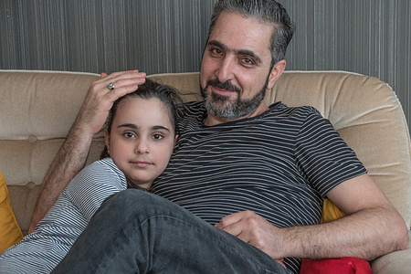 Syrian refugees - father and daughter, sitting together on a couch in their new Swedish home.