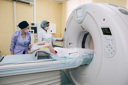 Patient lying down, undergoing a CT scan at a TB treatment ward in Moscow - two members of staff in surgical masks working the scanner.