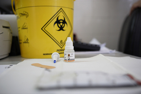A rapid HIV test sitting on a table in front of a biohazard disposal box.