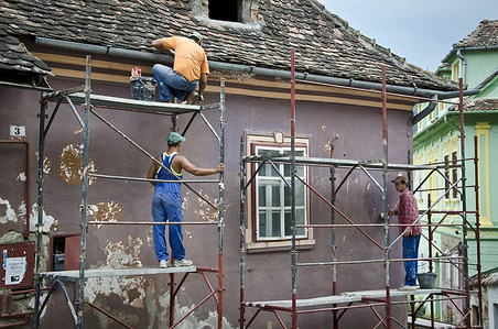 Three men standing on scaffolding, working on the exterior of a house.