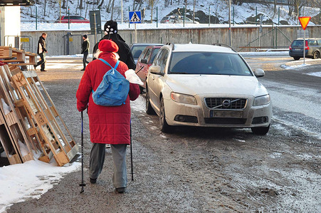 Elderly woman using walking sticks to walk outside on a winter day.